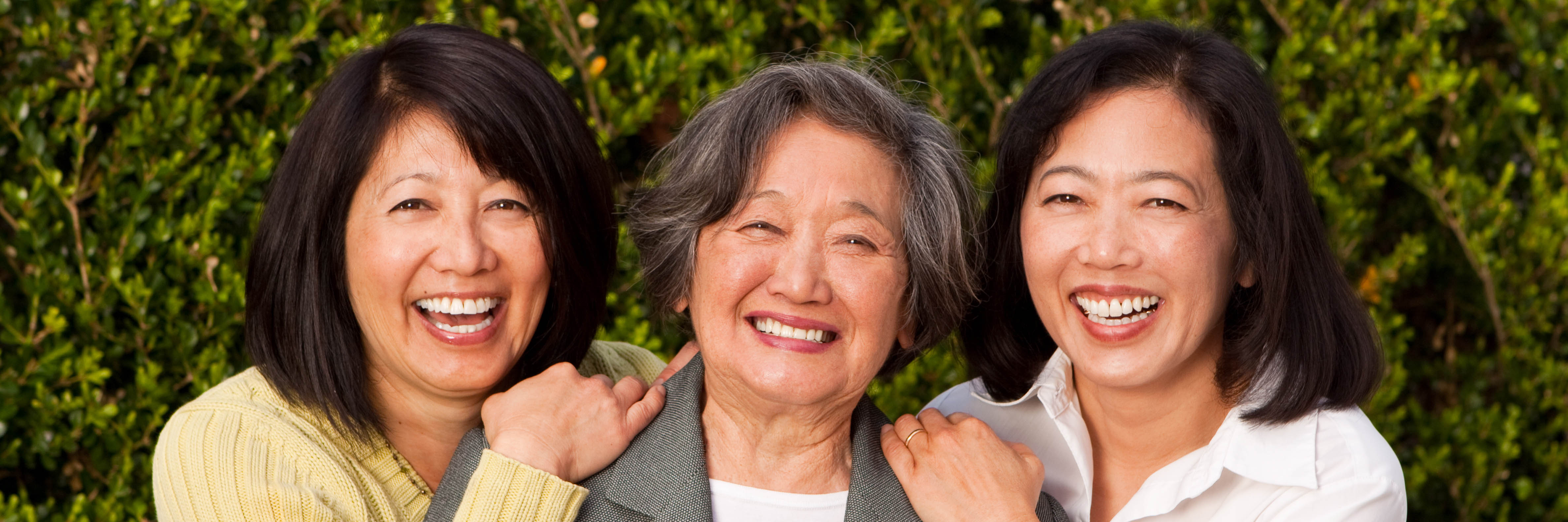 A mother and her two adult daughters, side-by-side, smiling outdoors.